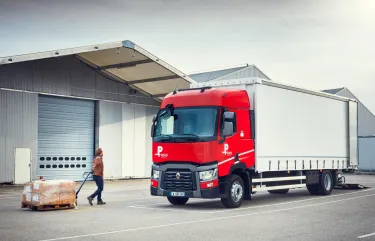 Man pulling a pallet truck towards a Renault Trucks P Road in front of a warehouse