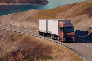 A Renault Trucks T tractor-trailer is traveling along a winding road overlooking a mountain lake.
