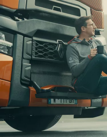 Model year 2025 : Renault Trucks T High Smart Racer : lifestyle (driver sitting on the windscreen access steps, relaxing with a cup in his hands)(Renault Trucks Stoneware Mug)(Renault Trucks Hero Zip Hoodie)